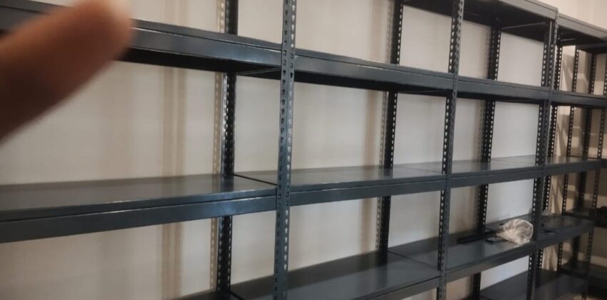 boltless rack of dark grey color installed at an office for storage purpose. 36 inches width, 15 inches depth, 5 shelves and 6feet height. wall is white in color.